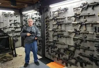 A man standing in front of a wall filled with guns.