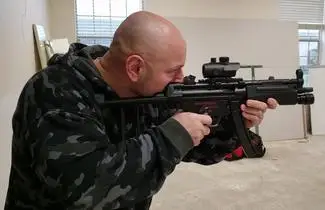 A man in camouflage jacket holding an automatic rifle.